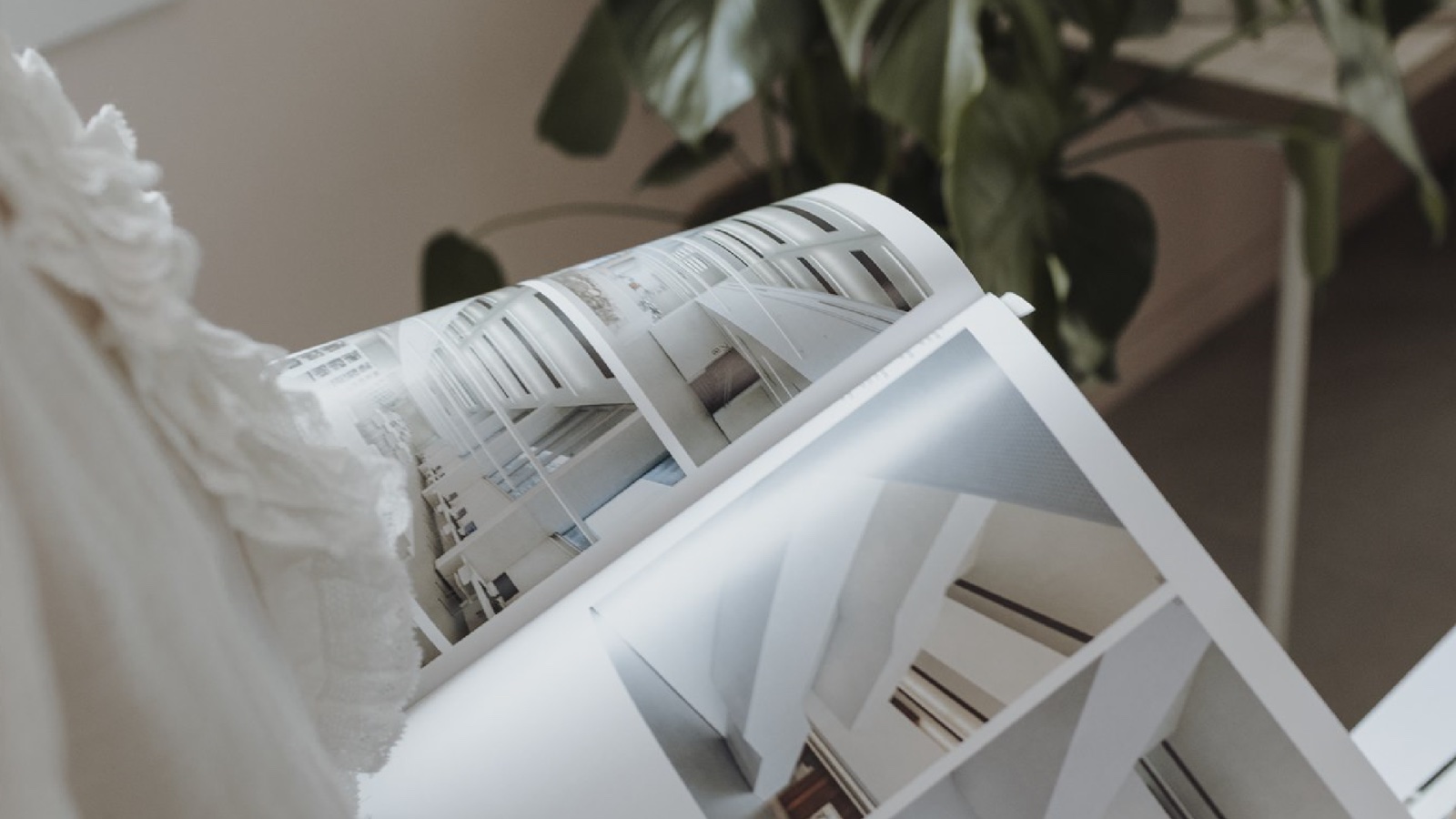 Rivista di arredamento sfogliata accanto a una pianta e a tessuti bianchi, tra le ispirazioni per scegliere lo stile della propria casa.